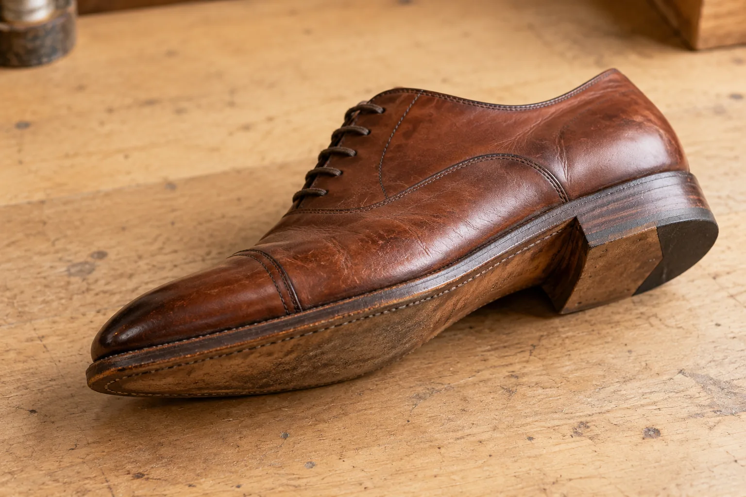 A brown leather Oxford on its side, showing the stitched welt, worn sole edge and stacked heel