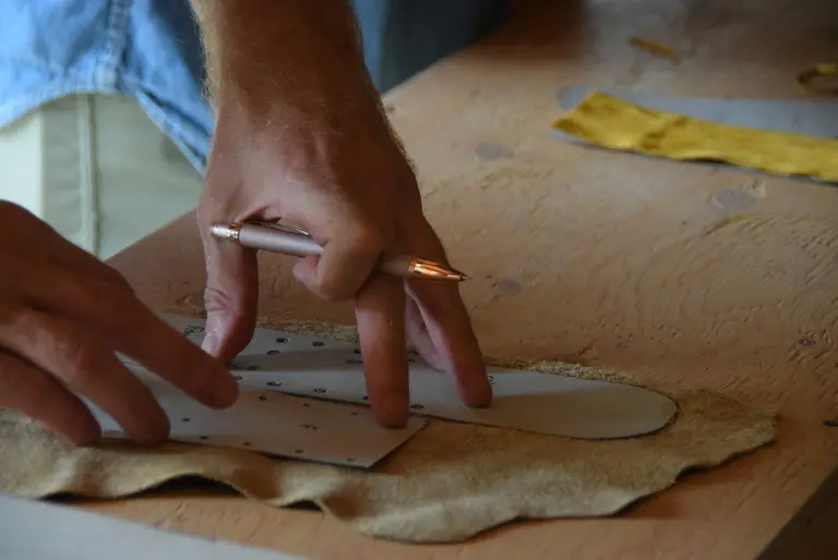 Hands marking a shaped piece of leather on a workbench