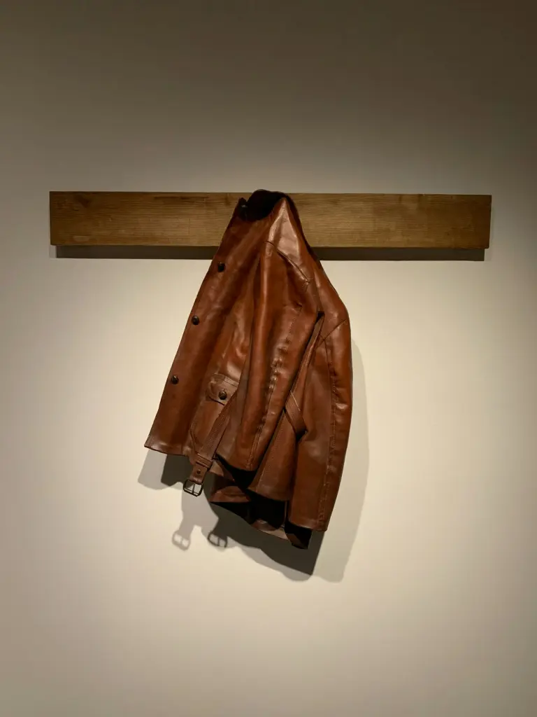 A brown leather jacket hanging from a wooden wall rail